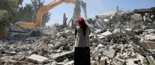 Seorang wanita Palestina menyaksikan alat berat milik otoritas Israel menghancurkan bangunan di wilayah Tepi barat Terjajah
